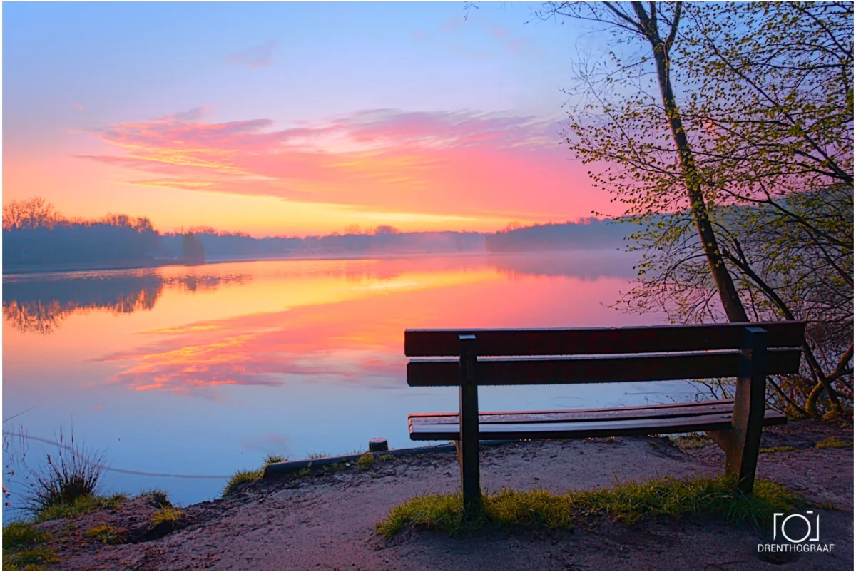 bankje aan een meer. De zon wolken aan de horizon worden prachtig aangelicht door de nog op te komen zon.