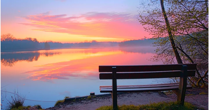 bankje aan een meer. De zon wolken aan de horizon worden prachtig aangelicht door de nog op te komen zon.